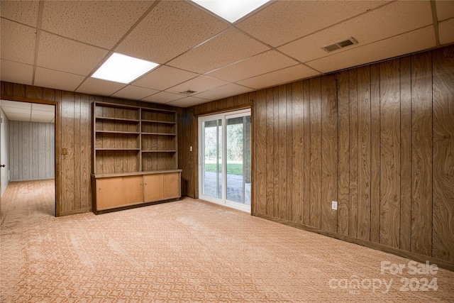 carpeted spare room featuring wood walls and a paneled ceiling