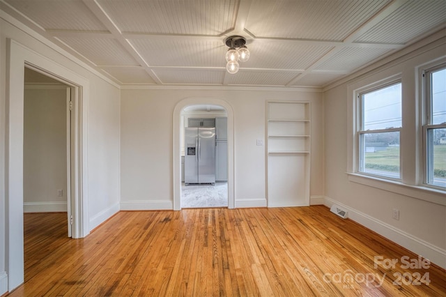 empty room featuring built in shelves, light wood-type flooring, and plenty of natural light