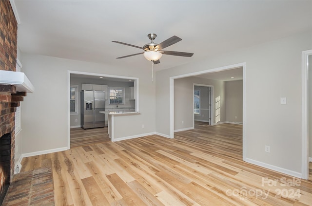 unfurnished living room with a brick fireplace, light wood-type flooring, and ceiling fan