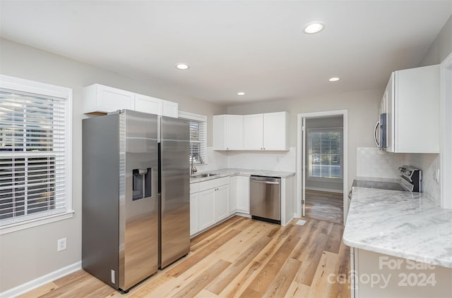 kitchen with stainless steel appliances, white cabinets, sink, light stone countertops, and light wood-type flooring