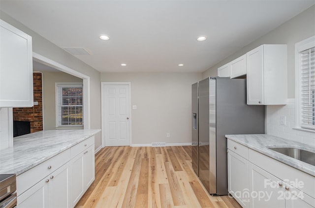 kitchen featuring tasteful backsplash, light stone counters, light wood-type flooring, stainless steel refrigerator with ice dispenser, and white cabinets