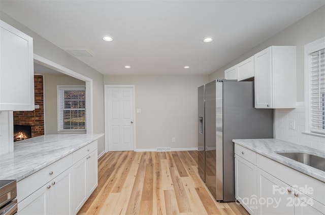 kitchen featuring stainless steel fridge, white cabinetry, light stone countertops, decorative backsplash, and light hardwood / wood-style flooring