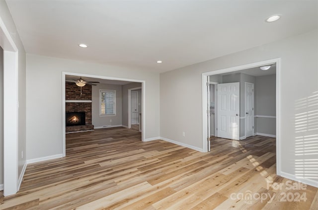 unfurnished living room featuring ceiling fan, a brick fireplace, and light hardwood / wood-style flooring