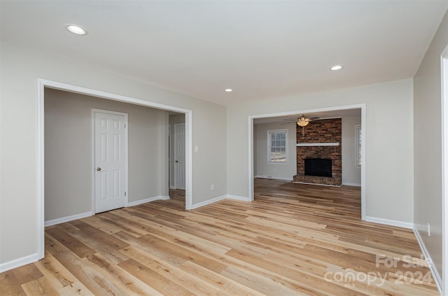 unfurnished living room featuring a brick fireplace, ceiling fan, and light wood-type flooring