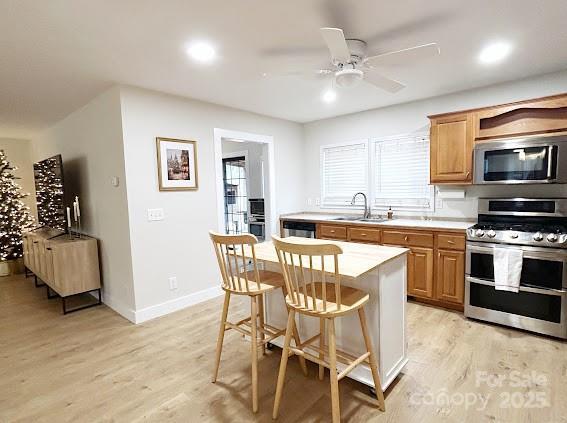 kitchen with ceiling fan, sink, a center island, a breakfast bar area, and appliances with stainless steel finishes