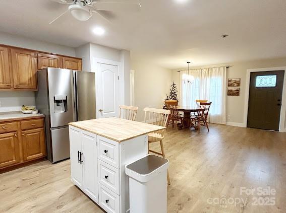 kitchen featuring a center island, light hardwood / wood-style flooring, stainless steel fridge, decorative light fixtures, and ceiling fan with notable chandelier