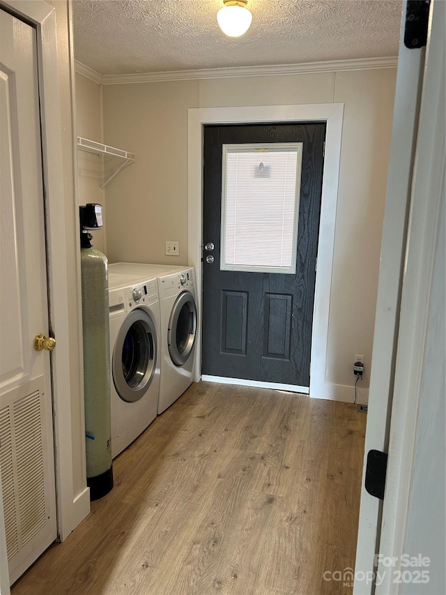 laundry room with washing machine and dryer, ornamental molding, a textured ceiling, and light wood-type flooring