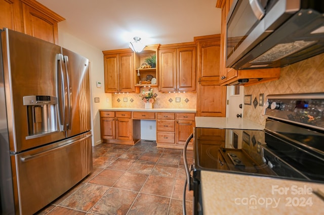 kitchen featuring appliances with stainless steel finishes, backsplash, and built in desk