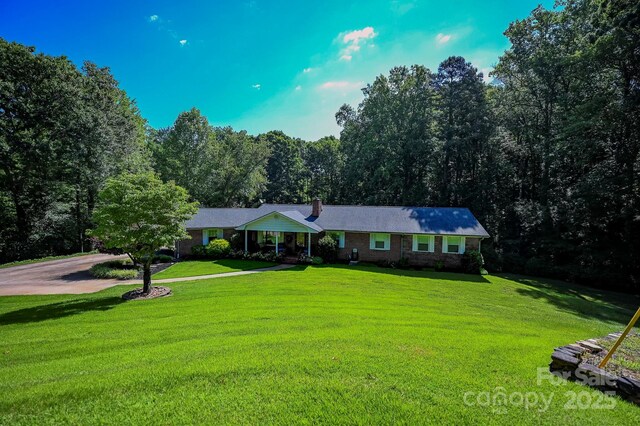 183 Creekside Dr, Forest City, NC 28043 - ranch-style house featuring a front yard, a chimney, brick siding, driveway, and a forest view