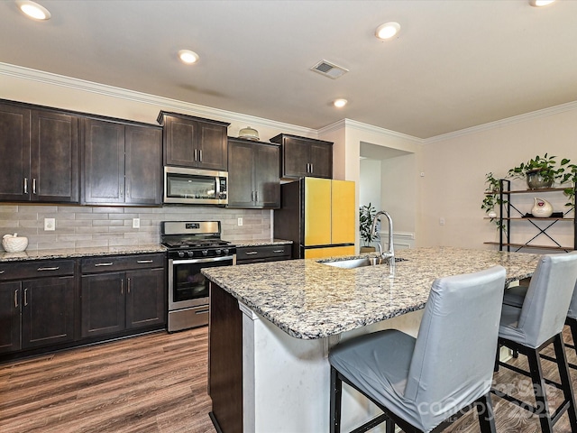 kitchen with stainless steel appliances, a kitchen island with sink, sink, dark hardwood / wood-style floors, and a breakfast bar area