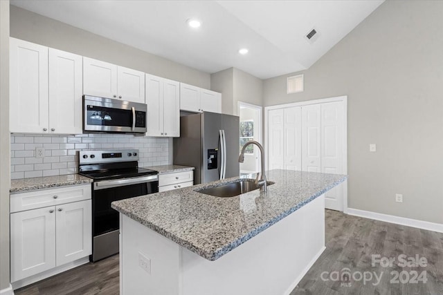 kitchen featuring white cabinets, stainless steel appliances, vaulted ceiling, and an island with sink