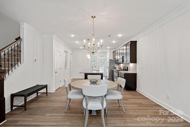 dining space featuring crown molding, sink, a chandelier, and light wood-type flooring