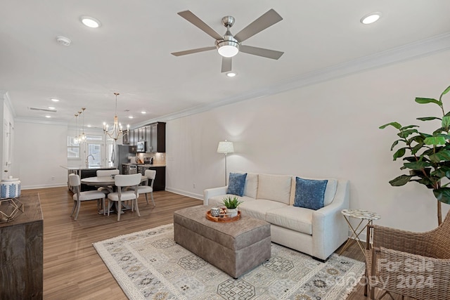 living room featuring ceiling fan with notable chandelier, sink, light wood-type flooring, and crown molding