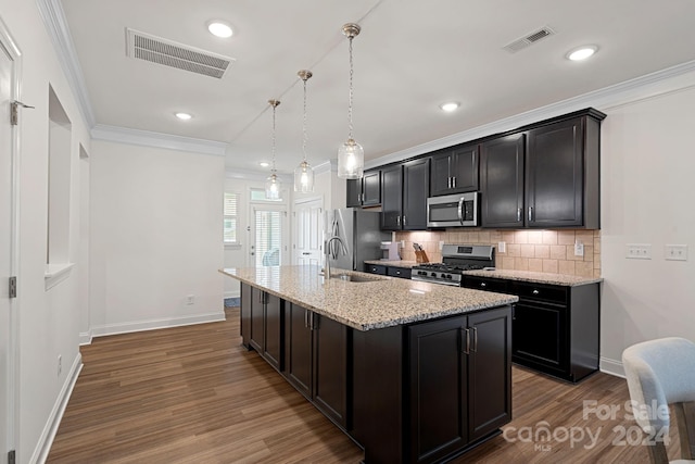 kitchen featuring appliances with stainless steel finishes, crown molding, sink, decorative light fixtures, and an island with sink