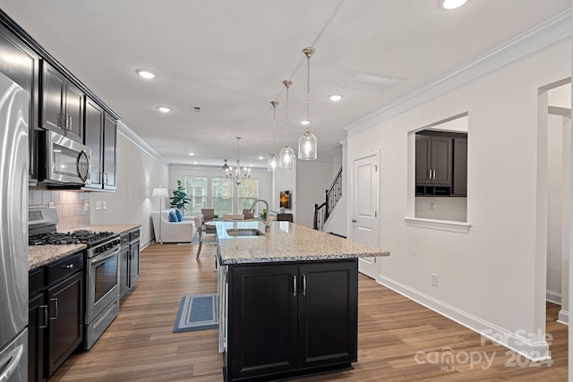 kitchen with a center island with sink, sink, hanging light fixtures, hardwood / wood-style flooring, and stainless steel appliances