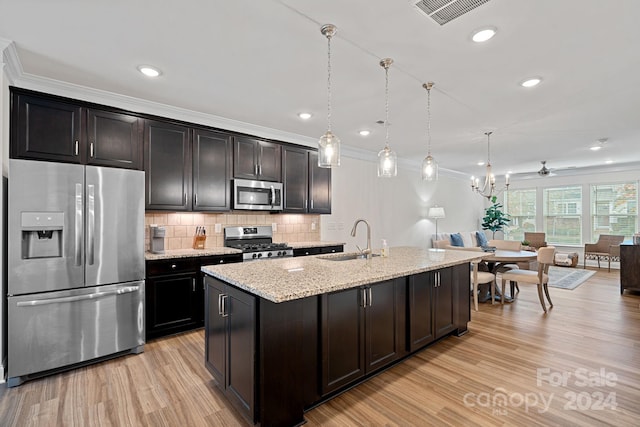 kitchen with a center island with sink, hanging light fixtures, crown molding, sink, and appliances with stainless steel finishes