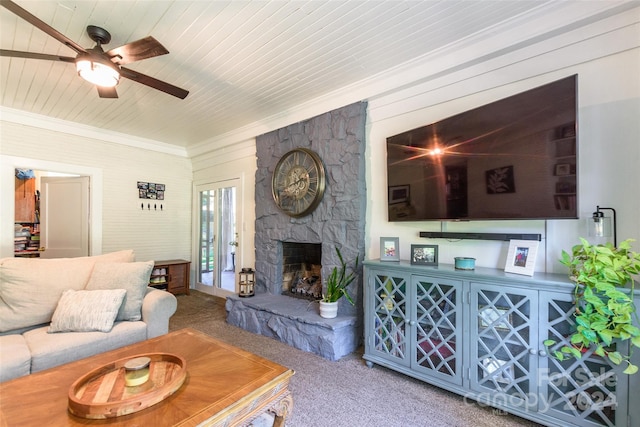 carpeted living room with ornamental molding, a stone fireplace, ceiling fan, and wooden ceiling