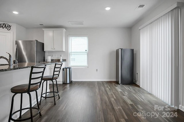 kitchen with dark stone counters, stainless steel refrigerator, dark hardwood / wood-style flooring, a breakfast bar, and white cabinets