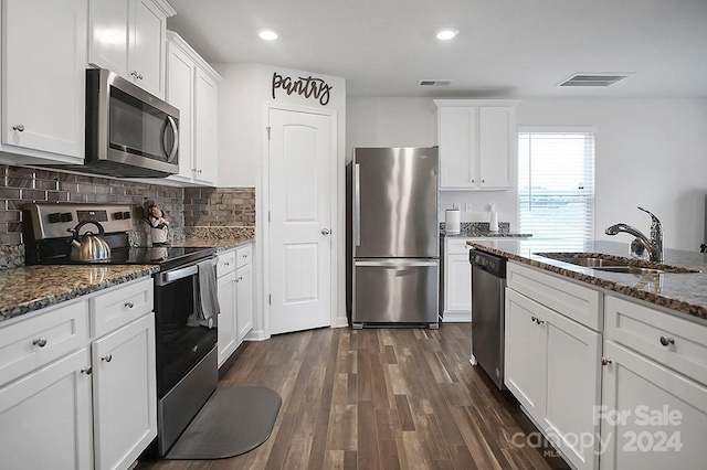 kitchen with stainless steel appliances, dark stone countertops, white cabinetry, and sink