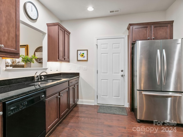 kitchen featuring stainless steel refrigerator, dishwasher, sink, dark wood-type flooring, and dark stone counters