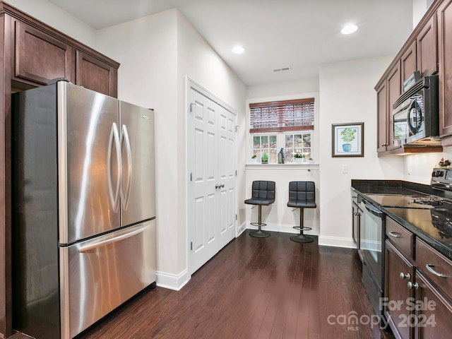 kitchen with dark brown cabinetry, dark hardwood / wood-style floors, black / electric stove, stainless steel fridge, and dark stone countertops