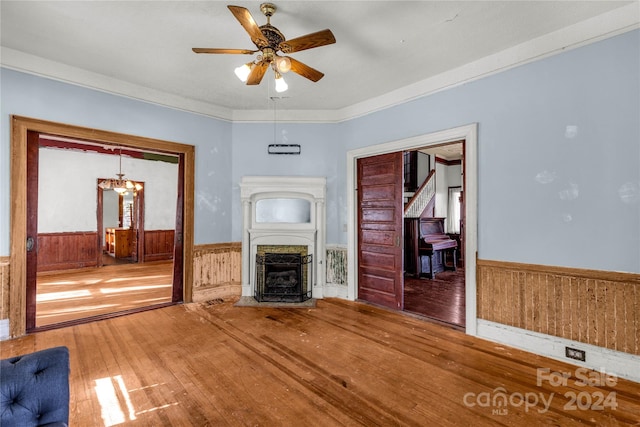 unfurnished living room with wood walls, hardwood / wood-style floors, and ceiling fan with notable chandelier