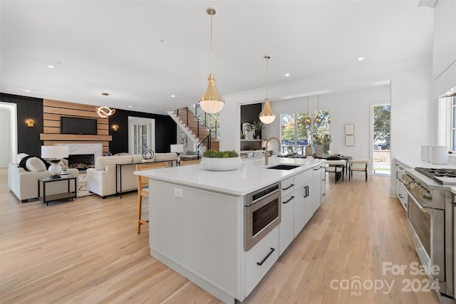 kitchen featuring white cabinetry, sink, hanging light fixtures, a kitchen island with sink, and light wood-type flooring