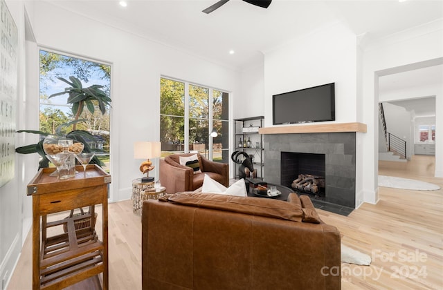 living room featuring hardwood / wood-style floors, ceiling fan, crown molding, and a tile fireplace