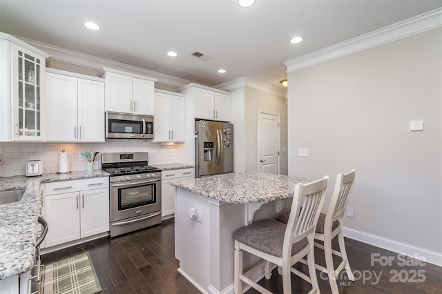 kitchen featuring decorative backsplash, a kitchen island, light stone counters, white cabinetry, and stainless steel appliances