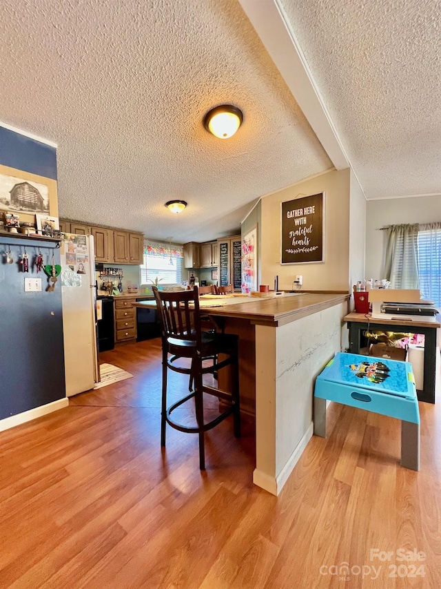 kitchen featuring white refrigerator, a textured ceiling, a breakfast bar, and kitchen peninsula