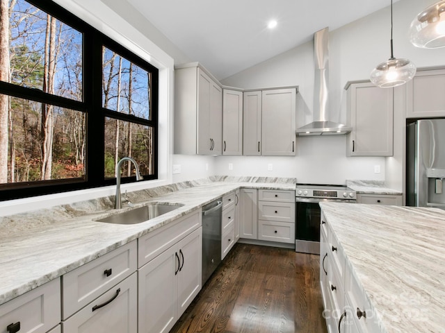 kitchen with appliances with stainless steel finishes, sink, white cabinets, hanging light fixtures, and wall chimney exhaust hood