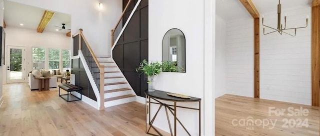 stairway with beamed ceiling, wood-type flooring, and an inviting chandelier