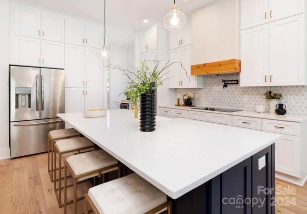 kitchen featuring pendant lighting, white cabinetry, black electric stovetop, and stainless steel fridge with ice dispenser