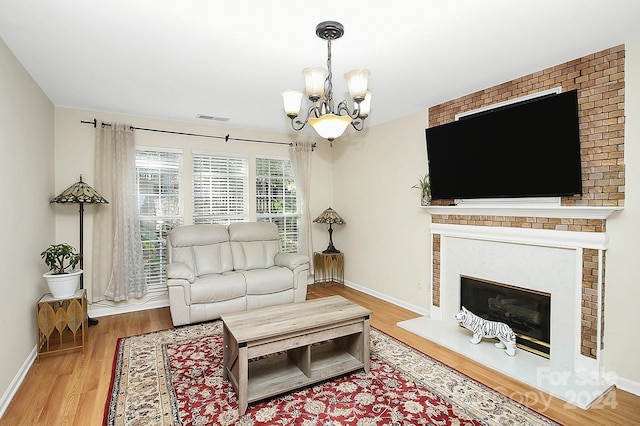 living room with a brick fireplace, wood-type flooring, and an inviting chandelier