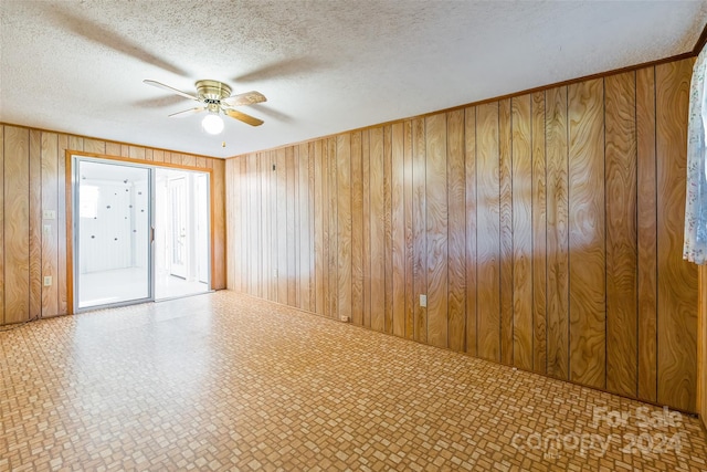 spare room with ceiling fan, a textured ceiling, and wooden walls