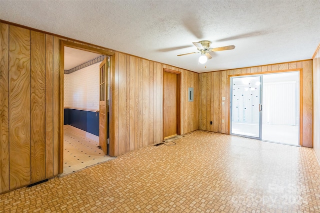 spare room with ceiling fan, wood walls, and a textured ceiling