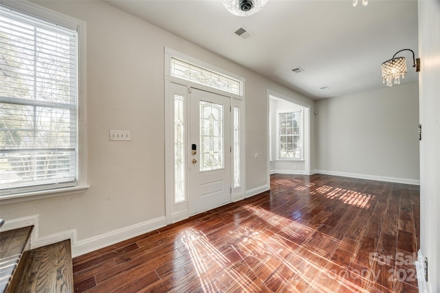 foyer entrance featuring a healthy amount of sunlight, dark hardwood / wood-style flooring, and a chandelier