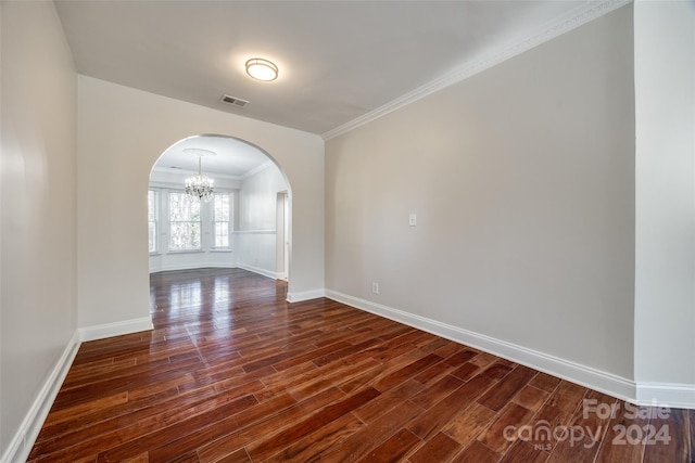 spare room featuring an inviting chandelier, dark wood-type flooring, and crown molding