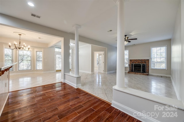 unfurnished living room featuring a fireplace, wood-type flooring, ceiling fan with notable chandelier, and ornate columns