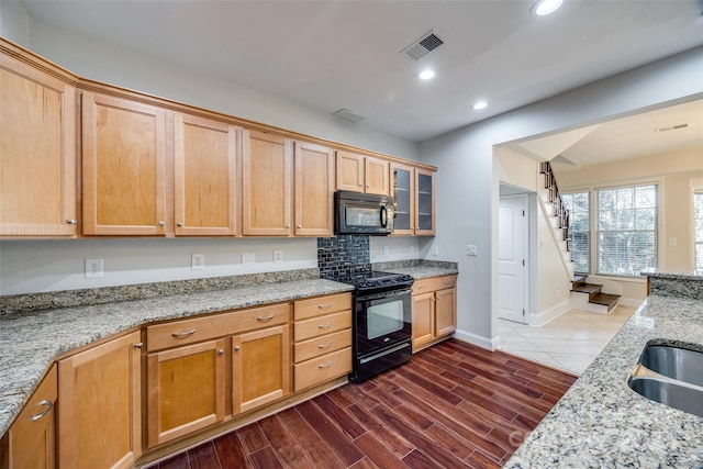 kitchen featuring black appliances, dark hardwood / wood-style floors, and light stone counters