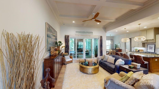 living room featuring beam ceiling, coffered ceiling, light wood-type flooring, ceiling fan with notable chandelier, and ornamental molding