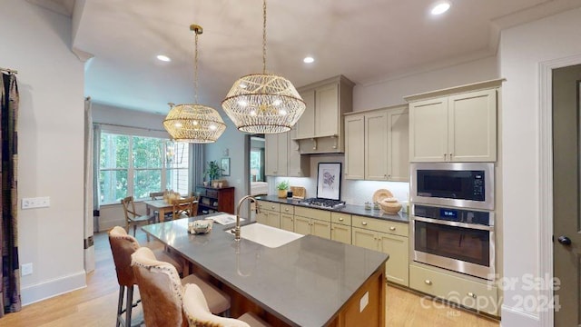 kitchen featuring stainless steel appliances, a kitchen island with sink, sink, decorative light fixtures, and a notable chandelier