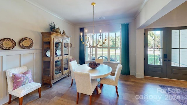 dining area with hardwood / wood-style floors, an inviting chandelier, ornamental molding, and french doors