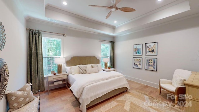 bedroom featuring ceiling fan, a raised ceiling, multiple windows, and light hardwood / wood-style flooring