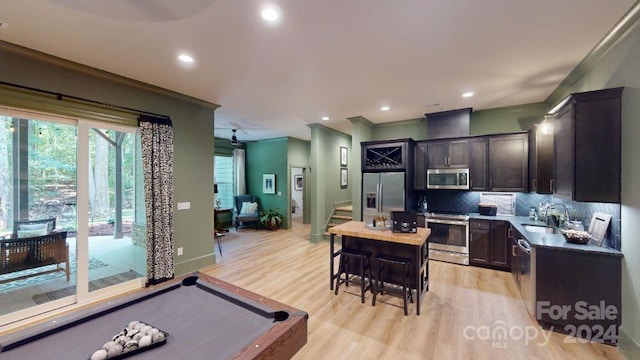 kitchen featuring sink, stainless steel appliances, decorative backsplash, a kitchen island, and light wood-type flooring