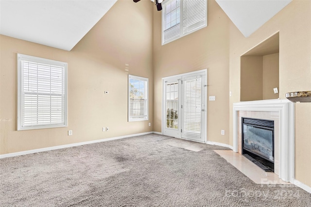 unfurnished living room with a high ceiling, light colored carpet, a wealth of natural light, and ceiling fan