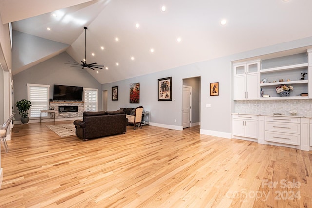 living room featuring ceiling fan, a stone fireplace, high vaulted ceiling, and light hardwood / wood-style flooring