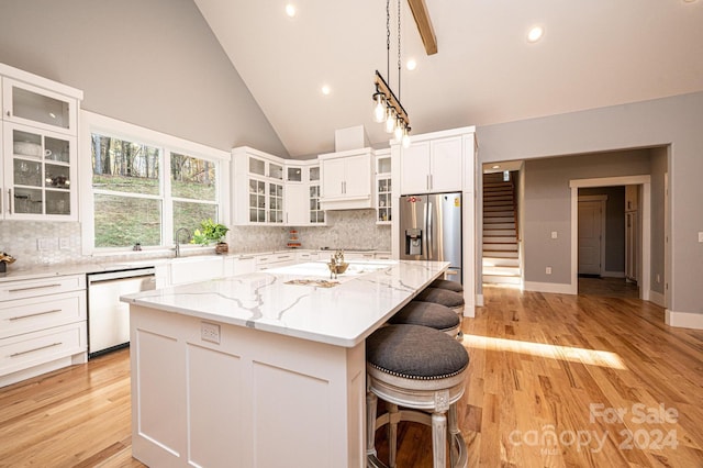 kitchen with high vaulted ceiling, light stone countertops, light wood-type flooring, a kitchen island, and stainless steel appliances