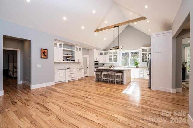 kitchen with pendant lighting, light wood-type flooring, a kitchen island, white cabinetry, and stainless steel refrigerator