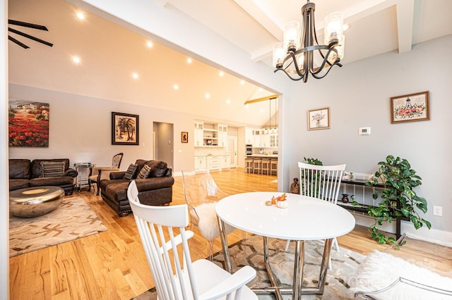 dining space with a notable chandelier, beam ceiling, light wood-type flooring, and high vaulted ceiling